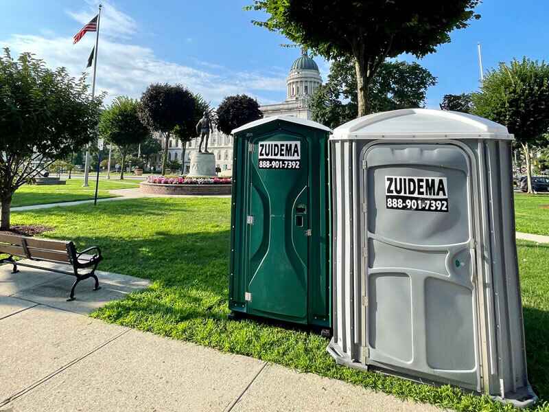 Park with two portableCrane Lift Restrooms on a paved area surrounded by greenery in NY and NJ