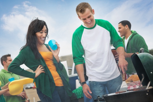 Two smiling friends grilling at a tailgate